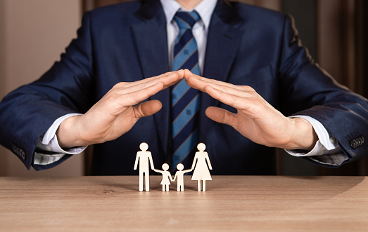A man in a suit holds hands in the shape of a house over the family. Insurance concept.