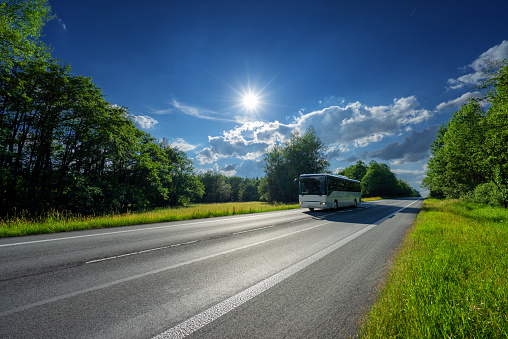 Tourist bus moves along a country road on summer sunny day