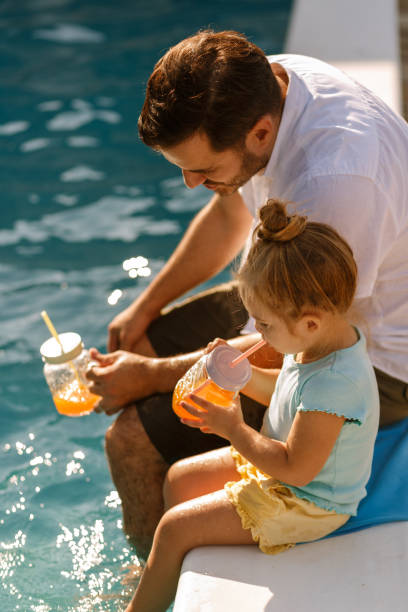 istock Bearded father and daughter enjoying fresh juice by the pool 1248630068