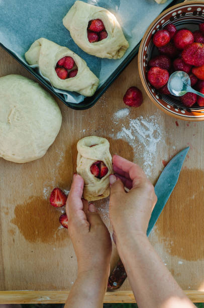 Women bake strawberry Buns. Dough on the table. Knead the dough. Female hands form a pie.
