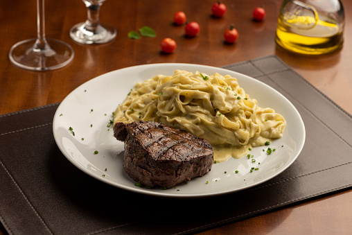 steak with pasta tagliatelle fetuccini on plate with blurred background with tomatoes olive oil and wine glass