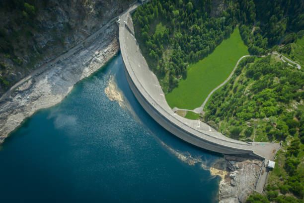 Aerial view of bridge on large dam in Swiss Alps Green landscape surrounds the dam and water, country road visible below reservoir photos stock pictures, royalty-free photos & images