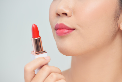 Beautiful young woman applying red lipstick on color background, closeup