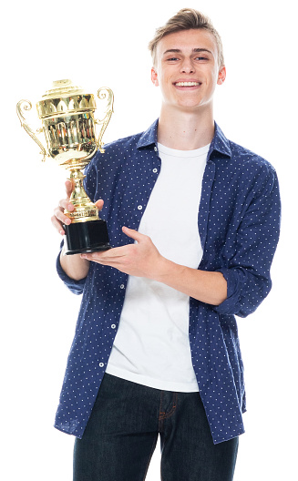 One person of aged 16-17 years old with short hair caucasian teenage boys standing in front of white background wearing pants who is successful and winning and showing award who is in first place and holding trophy