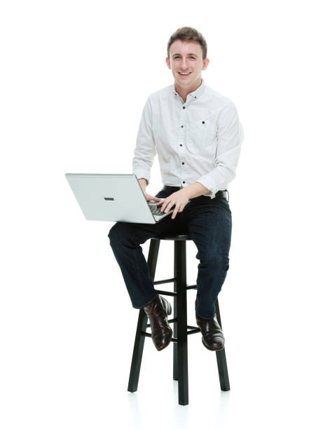 istock Caucasian male sitting in front of white background wearing jeans and using computer 1248657773