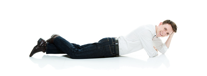 Profile view of aged 20-29 years old with brown hair caucasian male lying down in front of white background wearing pants who is smiling