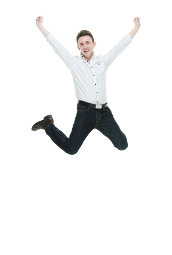 Front view of aged 20-29 years old with brown hair caucasian male jumping in front of white background wearing shirt who is feeling joy and showing arms outstretched with arms raised