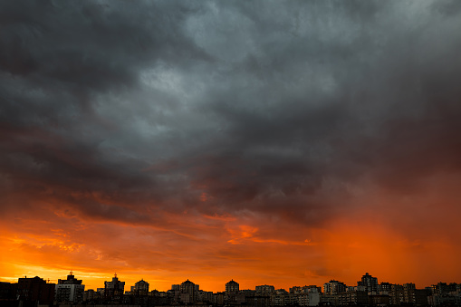 Dramatic stormy sunset sky with clouds over city skyline background.