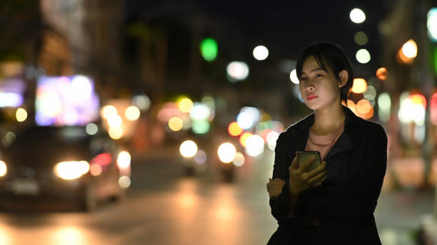 istock Asian woman requesting a ride with a smartphone in downtown city street at night 1248660607