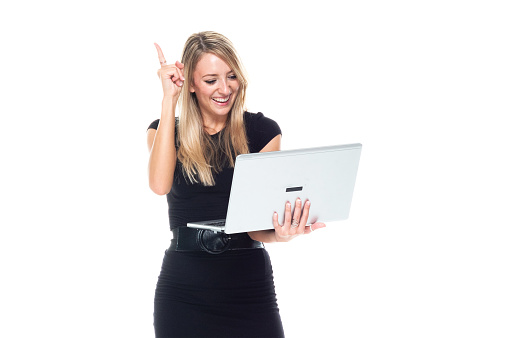 One person of aged 20-29 years old who is beautiful with long hair caucasian female businesswoman standing in front of white background wearing businesswear who is aspirations who is working and using laptop