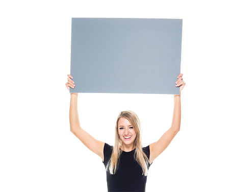 Waist up of aged 20-29 years old who is beautiful with long hair caucasian female businesswoman standing in front of white background wearing businesswear who is cheerful who is showing with hand and holding banner sign with copy space