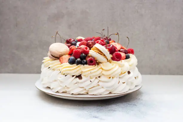 Photo of Pavlova meringue cake with fresh berries and macaroons on plain grey background. Copy space.