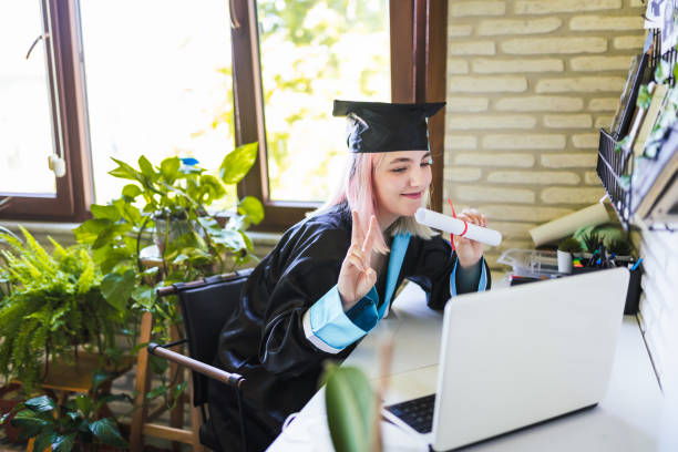 십대 소녀 착용 졸업 가운과 모자 인사 그녀의 가족 에 비디오 통화 - online degree 뉴스 사진 이미지