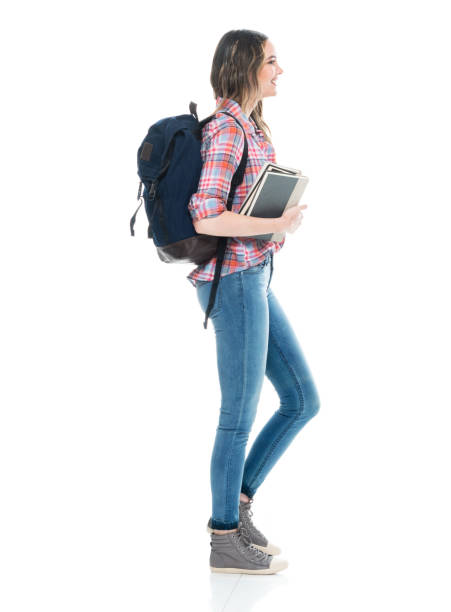 caucasian young women university student walking in front of white background wearing backpack and holding bag - adult education full length book imagens e fotografias de stock