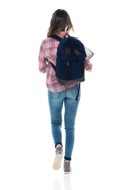 Caucasian female student walking in front of white background wearing backpack and holding book Rear view of aged 20-29 years old who is beautiful caucasian female student walking in front of white background wearing backpack who is studying and holding book human back photos stock pictures, royalty-free photos & images