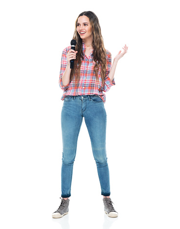 Full length of aged 20-29 years old who is beautiful caucasian female standing in front of white background wearing plaid shirt who is giving speech and holding microphone