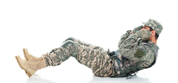 Side view of aged 30-39 years old who is tall person with black hair caucasian male army soldier doing sit-ups in front of white background in the army wearing military uniform who is in concentration and showing patriotism and being active with sports training