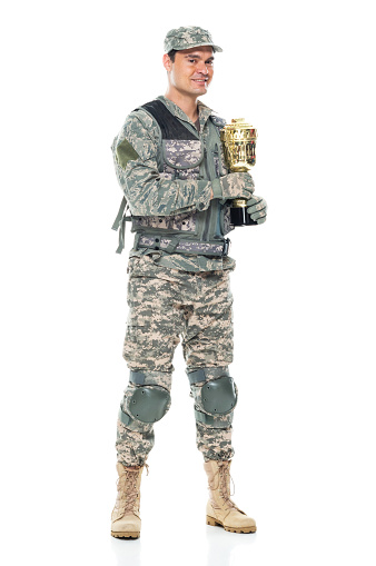 Full length of aged 30-39 years old who is tall person with black hair caucasian male armed forces standing in front of white background in the military wearing uniform who is successful and winning and showing award who is in first place and holding trophy