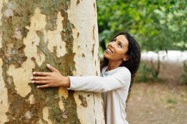 Young woman nature lover hugging a tree Young woman nature lover hugging the trunk of a large tree outdoors in a garden or park looking up with a happy contented smile hugging tree stock pictures, royalty-free photos & images
