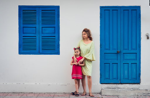 Mother and daughter next to shutter window in a street