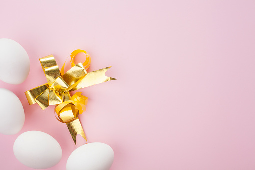 White eggs on a pink background, decorated with a gold bow, with copy space. Easter concept.