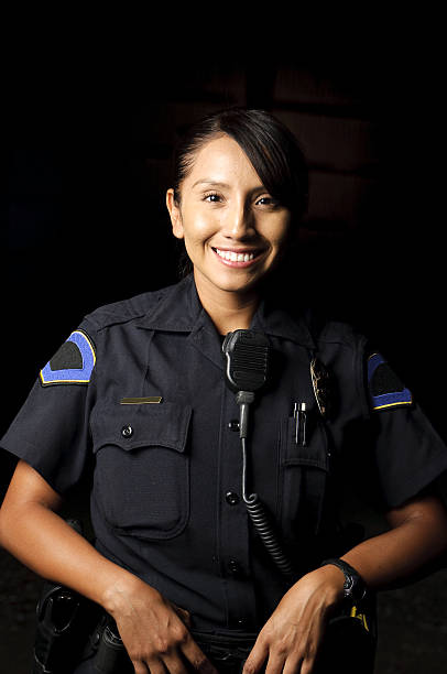 police officer a Hispanic female police officer standing in the dark and smiling. female police officer stock pictures, royalty-free photos & images