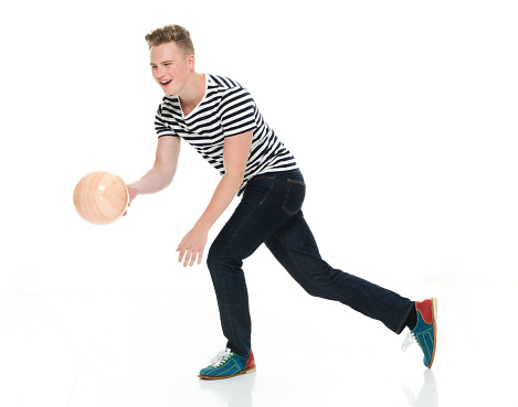 Profile view of aged 18-19 years old caucasian young male walking in front of white background wearing jeans who is smiling who is throwing and using sports ball