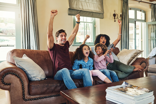 Shot of a beautiful young family of four celebrating while watching tv together at home