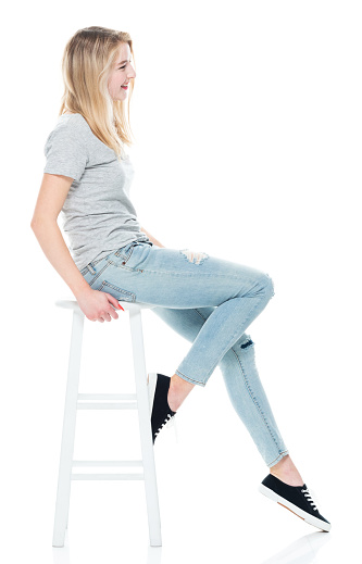 Side view of aged 18-19 years old who is beautiful with long hair generation z young women sitting in front of white background wearing jeans who is cheerful