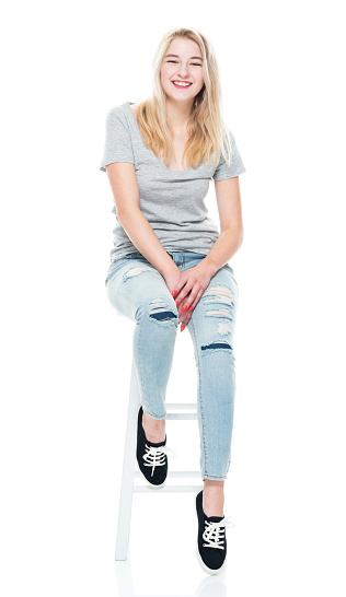 Full length of aged 18-19 years old who is beautiful with long hair caucasian teenage girls sitting in front of white background wearing canvas shoe who is laughing