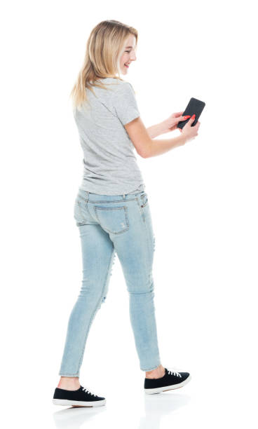 Generation z female in front of white background wearing t-shirt and using smart phone Rear view of aged 18-19 years old who is beautiful with blond hair generation z female in front of white background wearing t-shirt who is showing cool attitude and using smart phone pics of girls buttocks stock pictures, royalty-free photos & images