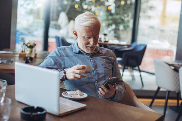 istock Mature businessman using mobile phone. Mid adult entrepreneur using mobile phone at restaurant. Confident and smiling businessman working on mobile phone at restaurant. 1248691348
