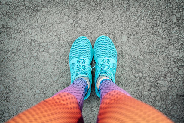 Selfie of female legs in blue sneakers and multi-colored leggings on the pavement Selfie of female legs in blue sneakers and multi-colored leggings on the pavement, top view personal perspective standing stock pictures, royalty-free photos & images