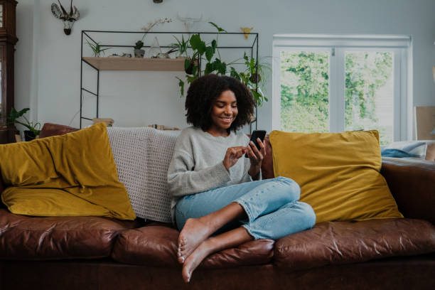 bella donna con afro su smartphone a casa nel salone - woman phone foto e immagini stock