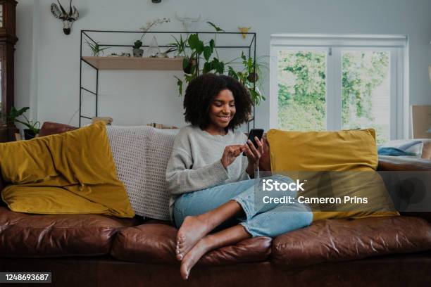 Beautiful Woman With Afro On Smartphone At Home In The Lounge Stock Photo - Download Image Now