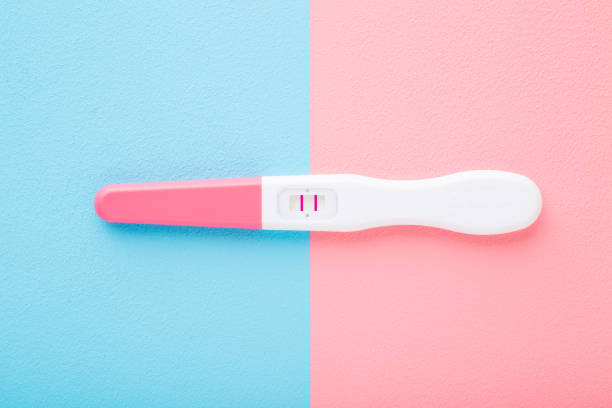 istock Pregnancy test with two stripes on light pink blue table background. Pastel color. Positive result. Closeup. Two sides. Top down view. 1248695713