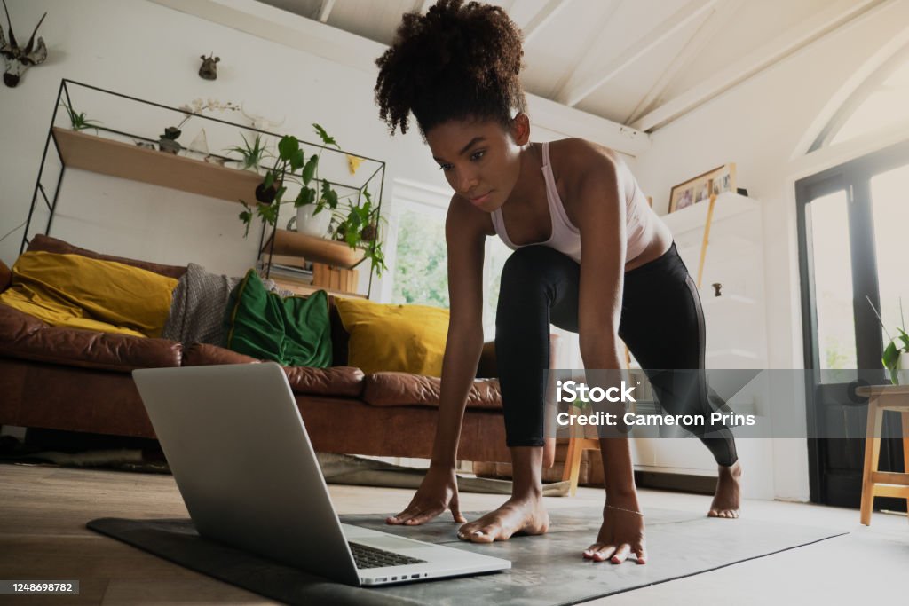 Beautiful young mixed race woman working out from home, online workout on laptop Beautiful young mixed race female exercising at home, online workout on laptop Exercising Stock Photo
