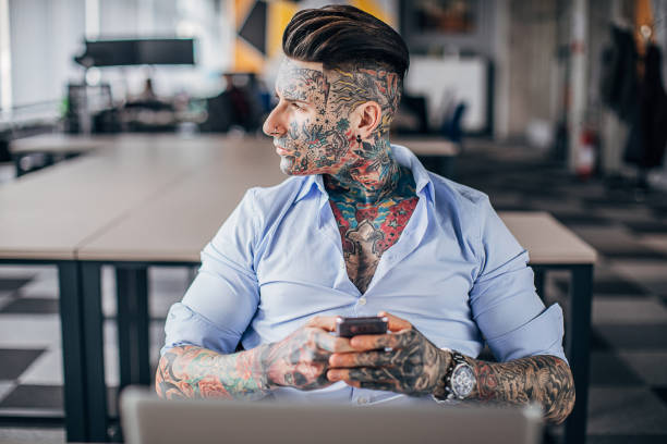 istock Businessman with whole body covered in tattoos using mobile in office 1248699345