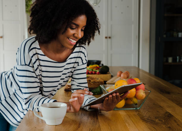 Young female in the kitchen scrolling and browsing on touch pad or tablet with cup of coffee
