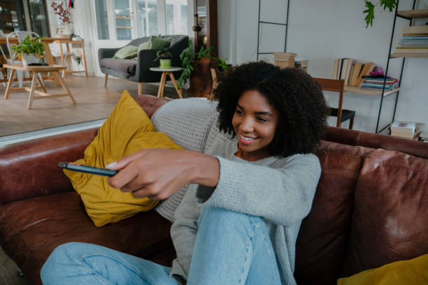 istock Beautiful woman scrolling on tv remote control while sitting in the lounge 1248701144
