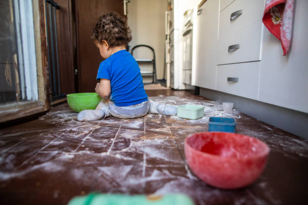 Son playing with flour at kitchen while mom is not at home Rear view of toddler boy sitting on floor and making a mess with flour at kitchen flour mess stock pictures, royalty-free photos & images