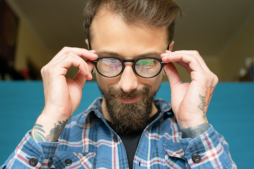 Attractive young bearded man with rose tattoo wearing eyeglasses. Guy looking at laptop screen and sitting on isolation. Working at home and freelance concept