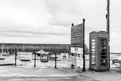 Minehead Somerset England UK beach and harbour at low tide with boats moored in the sand on a wet and blustery day. In the foreground is an old telephone box and information signs on parking and the harbour history.