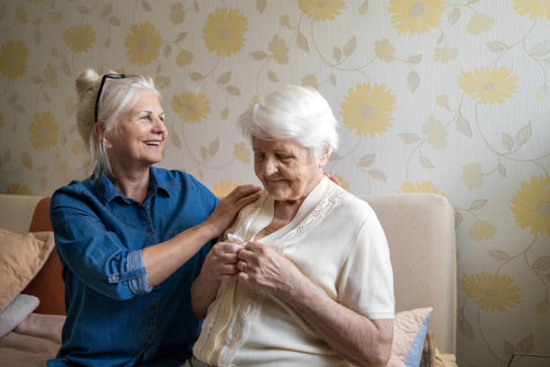 женщина помогает старшей женщине одеваться в своей спальне - senior adult home caregiver help care стоковые фото и изображения