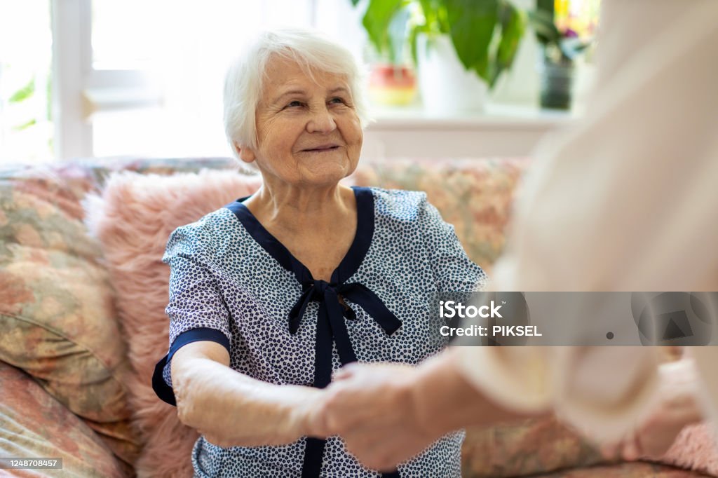 Female home carer supporting old woman to stand up from the sofa at care home Senior Adult Stock Photo