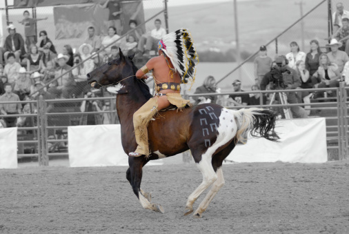 Tribal Chief Wearing Full Headress. Riding Bareback on Painted Pony. Background black & white.