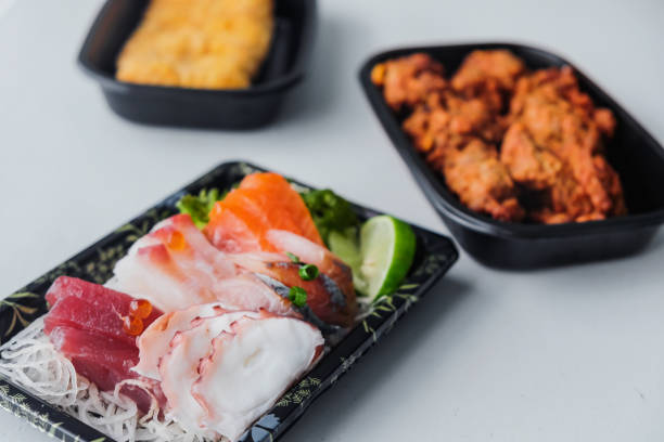 Close up shot set of healthy Japanese takeout meal which consists chicken karaage,  chicken katsu and variation raw sashimi above dining table, ready to eat during  Covid 19 lockdown
