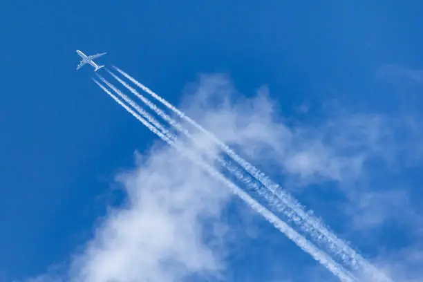 Four engined airliner flying at high altitude above the clouds with a large contrail forming behind it.