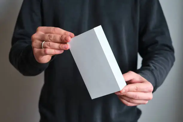 Photo of Man holding in hand small paper box. Blank packing, empty space. Male with a new package. Postal service, delivery. White paper. Gift box, present. Box close up. People communication. Carton case