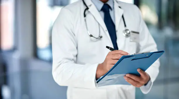 Cropped shot of an unrecognisable doctor writing notes in a folder in a modern hospital